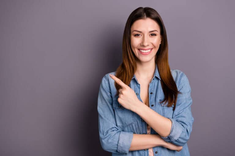 Woman pointing to her smile after cosmetic dentistry treatment in Colorado Springs, CO