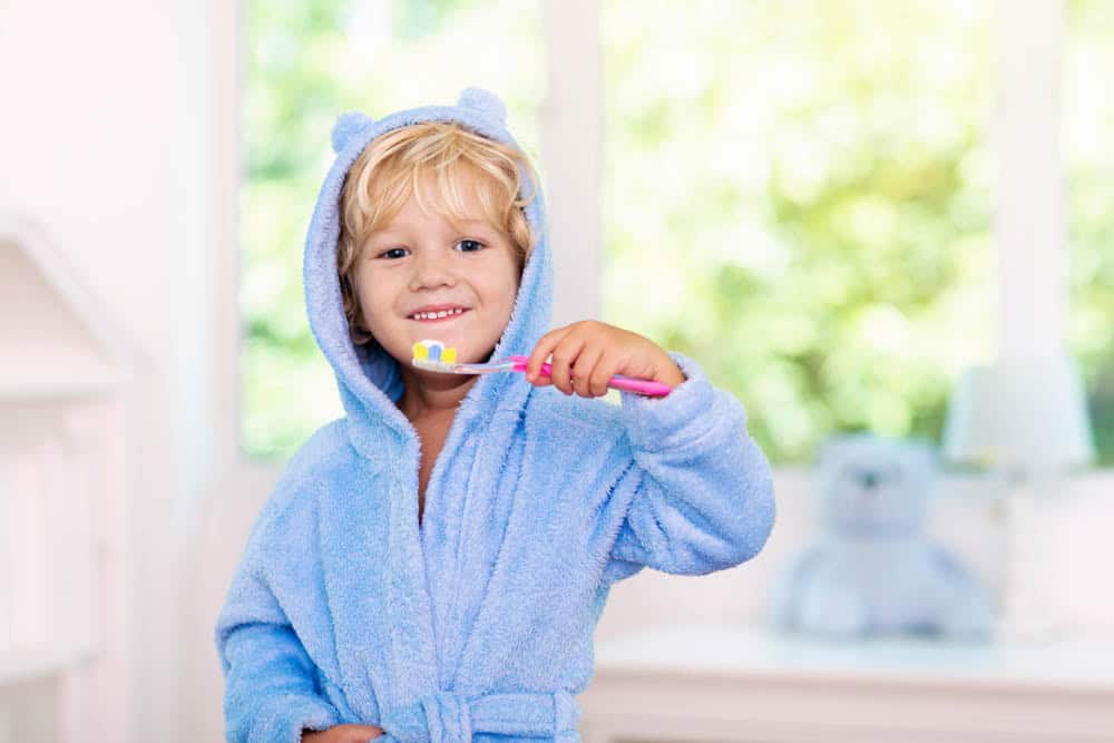 Young child brushing teeth happily to build positive dental habits and reduce dental anxiety