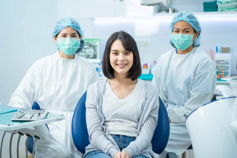 Young woman in dental chair with two dental staff members during routine dental exam in Colorado Springs