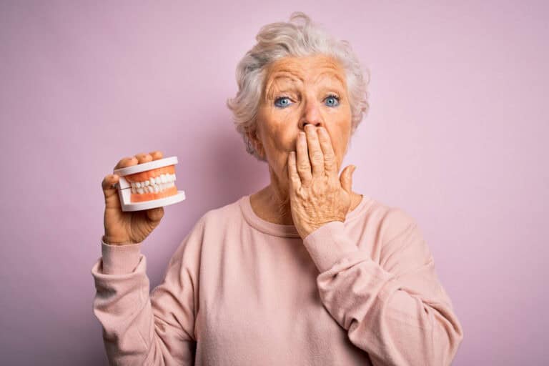Senior woman holding dentures demonstrating proper denture aftercare in Colorado Springs, CO