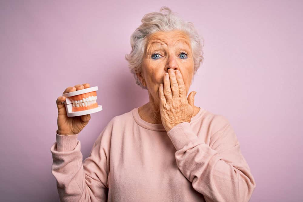 Senior woman holding dentures demonstrating proper denture aftercare in Colorado Springs, CO