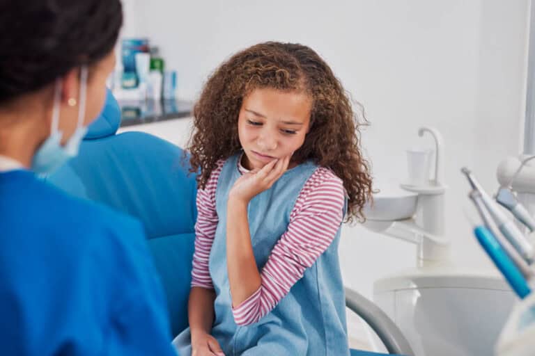 Girl holding cheek nervously in dental chair representing tips to ease dental anxiety in Colorado Springs