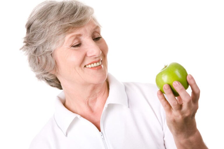 Older woman biting into green apple after replacing missing teeth in Colorado Springs, CO