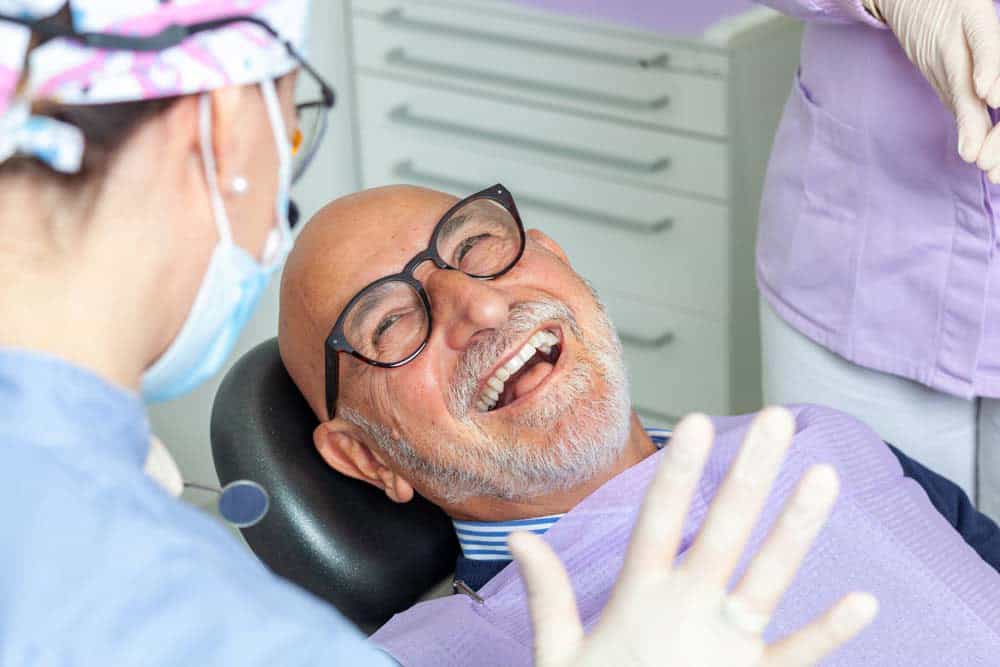 Senior male patient laughing comfortably in dental chair after successful root canal treatment
