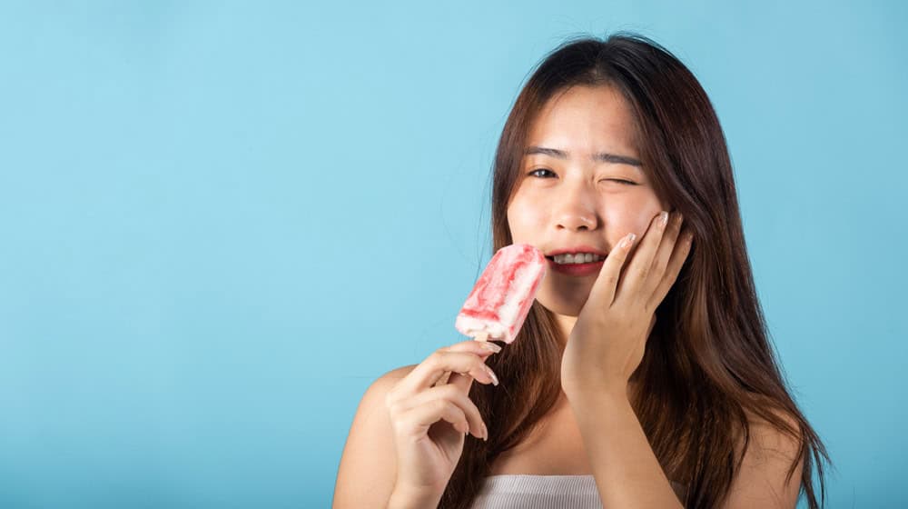Woman wincing with sensitive teeth eating ice cream showing worst foods for oral health